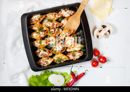 Italienische Pasta Conchiglioni Rigati gefüllt mit Käse und Fleisch auf weißem Holz Tisch. Ansicht von oben. Stockfoto