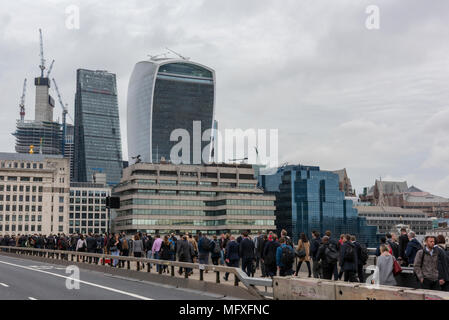 Pendler verpackt auf dem Gehsteig durchqueren London Bridge in der Londoner City während der morgendlichen Rush hour mit Stadt ikonischen Gebäude der Skyline. Stockfoto