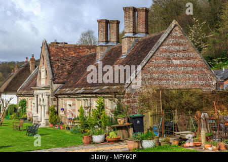 Armenhäuser in Milton Abbas in Dorset, England, UK, GB mit traditionellen Englischen strohgedeckten Häuser entlang der Straße mit begrünt Verges. Stockfoto