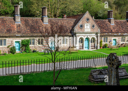 Armenhäuser in Milton Abbas in Dorset, England, UK, GB mit traditionellen Englischen strohgedeckten Häuser entlang der Straße mit begrünt Verges. Stockfoto