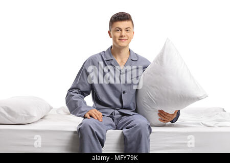 Teenager im Schlafanzug sitzt auf einem Bett und einem Kissen auf weißem Hintergrund Stockfoto