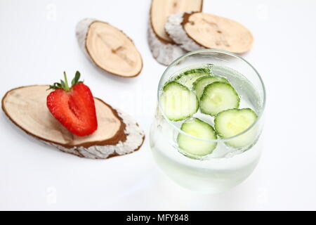 Detox aromatisiertes Wasser mit Gurke auf weißem Hintergrund mit roten Erdbeere und Holz Dekoration. Gesunde Ernährung Konzept. Anti stress Trinken Stockfoto