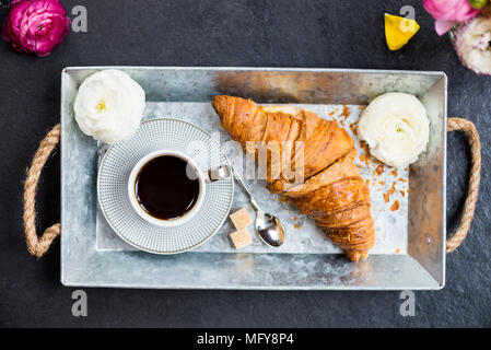 Leichtes Frühstück aus frischen Croissant und Kaffee auf der grauen Fach, Ranunculus Blumen in der Nähe Stockfoto