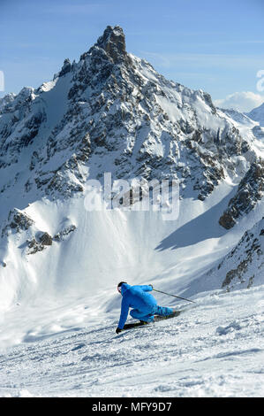 Ein Skifahrer schnitzt eine Umdrehung auf der Piste vor der Aiguille du Obst Berg in den Französischen Alpen Courchevel. Stockfoto