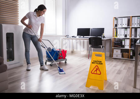 Weibliche Hausmeister Reinigung Büro mit nassen Boden Warnschild auf dem Boden Stockfoto