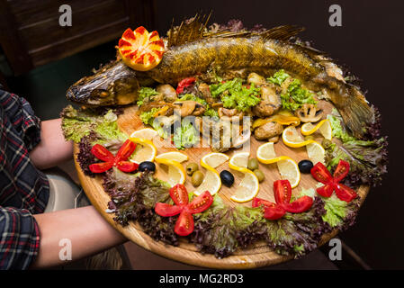 Der Kellner hält eine große Diele mit einem großen leckeren gebackenen Fisch und Gemüse Stockfoto