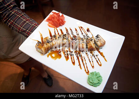 Golden Dragon sushi Rollen mit Thunfisch, Aal, Gurke, Sesamsamen auf einem weißen Teller mit Wasabi und imbrem in die Hände des Kellners Stockfoto
