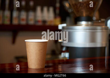 Einen Pappbecher mit Kaffee auf einer hölzernen Zähler vor dem Hintergrund einer unscharfen Bar. Stockfoto