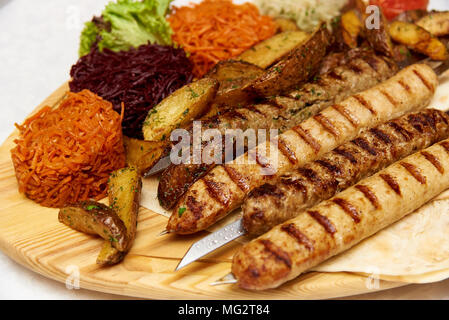 Gericht aus Hammel- Hackfleisch in Form von kleinen gebratene Würstchen mit scharfen Gewürzen auf pita Brot und Gemüse auf einem Holzbrett Stockfoto