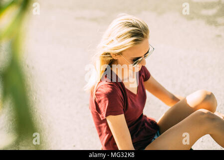 Moderne junge blonde Mädchen lächeln, sitzt auf einem Skateboard Stockfoto