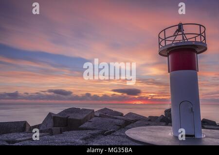 Magentafarbene sunrise mit der Sonne peeking über dem Horizont. Light Tower im Vordergrund und leichte Cloud Bewegung verwischen. Alle am Meer. Stockfoto