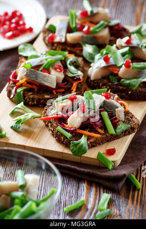 Bruschetta auf Roggenbrot mit gebratenen Strohhalme für Zuckerrüben und Karotten, grüne und Scheiben Hering auf der Bambus. Stockfoto