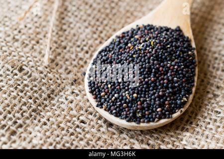 Schwarze Senfkörner in Löffel aus Holz mit Sack. Organisches Produkt. Stockfoto