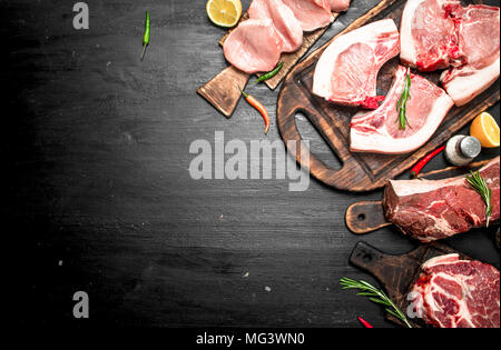Verschiedene Arten von rohem Schweinefleisch und Rindfleisch mit Kräutern und Gewürzen. Auf der schwarzen Tafel. Stockfoto