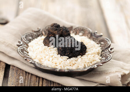 Schwarze Trüffel und Reis auf dem Teller auf alten Holztisch. Stockfoto