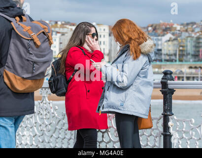Zwei junge Frauen, die auf einem Pier am Meer, eine Rede auf einem Smartphone, während die anderen Arten einen Text oder verwendet eine App auf Ihr Mobiltelefon. Stockfoto