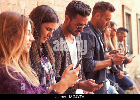 Große Gruppe von Freunden über Smart Phone gegen eine Rote Wand aus Ziegel - junge Menschen durch Mobile Smartphone süchtig-Technologie millennials Konzept Stockfoto
