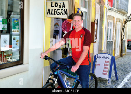 Jungen blonden Mann mit der portugiesischen Nationalmannschaft shirt sitzt auf einem Fahrrad und lächelnd in die Kamera Stockfoto