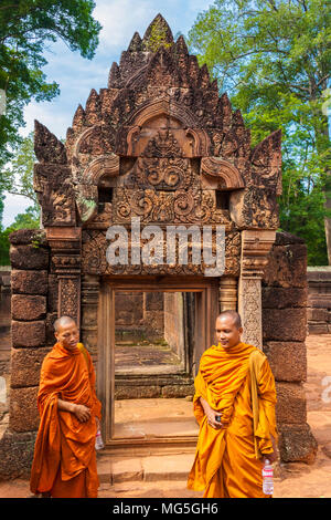 Zwei Buddhistische Mönche, in einem gelben und orangefarbenen Robe, stehen vor der Tür, eine Galerie in der zweiten Gehäuse der Kambodschanischen Banteay Srei. Stockfoto