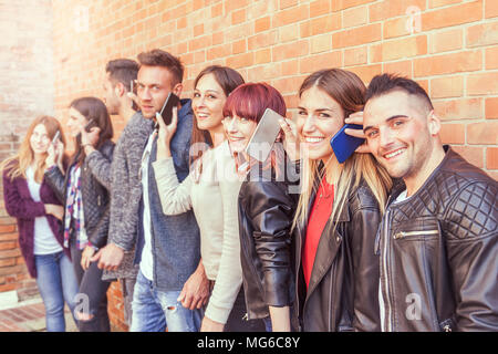 Große Gruppe von Freunden über Smart Phone gegen eine Rote Wand aus Ziegel - junge Menschen durch Mobile Smartphone süchtig-Technologie millennials Konzept Stockfoto