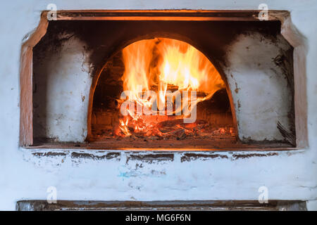 Russischen Ofen weiß lackiert mit schmutzigen geräuchert Flecken. Das Verbrennen von Holz im Kamin. Mauerwerk Herd zum Kochen und Heizen verwendet. Stockfoto