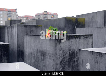 Helle Blumenstrauß auf grauem Beton Kontraste mit repressiven feuchten grauen Stein von Holocaust Mahnmal Berlin Deutschland Stockfoto