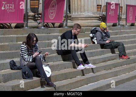 Glasgow, Schottland, Großbritannien, 27.April. UK Wetter: junge Leute sitzen auf Schritte texting mit Telefonen Sonnenschein in die Stadt kommt, wie die Einheimischen und Touristen das heiße Wetter in Royal Exchange Square, im Herzen der Stadt. Gerard Fähre / alamy Nachrichten Stockfoto