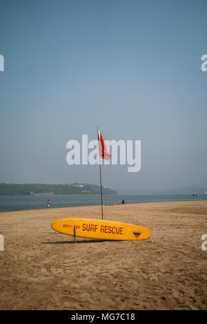 Eine gelbe Surfboard und eine rote Flagge auf einem Strand in Goa, Indien Stockfoto