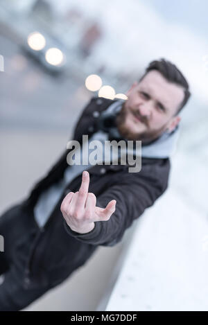 Ein hübscher junger hipster Mann seinen Mittelfinger in die Kamera im städtischen Umfeld. Stockfoto