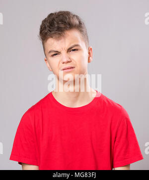 Emotionales Porträt der kaukasischen umgekippt Problem jugendlich Junge. Traurige junge Blick auf Kamera. Sorgen Kind tragen rote t-shirt, auf grauem Hintergrund. Stockfoto