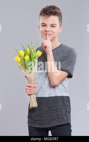 Jugendlich junge ausblenden Blumen hinter sich, auf grauem Hintergrund. Kind mit Strauß gelber Tulpen als Geschenk. Glückliche Mütter, Geburtstag oder Valentin Stockfoto