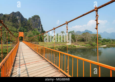 Orange suspension Brücke über den Fluss Nam Song und malerischen Kalkstein Karst Berge in der Nähe von Tham Chang (oder Jang oder Jung) Höhle in Vang Vieng, Laos. Stockfoto