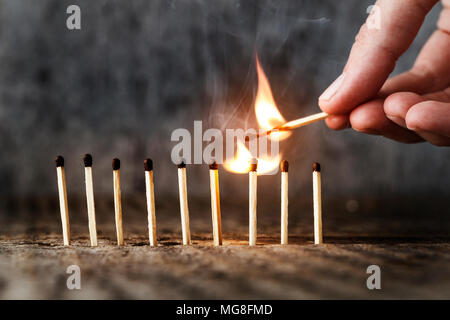 Matches stehen in einer Reihe, eine Übereinstimmung brennt. Ein Mensch setzt eine Übereinstimmung in Brand. Konzept der Idee. Platz für Text Stockfoto