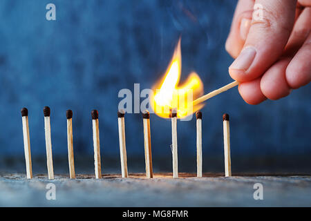 Gleiche in einer Reihe auf einem hölzernen Hintergrund, eine Hand mit einem brennenden Streichholz legt Feuer zu einem anderen überein. Stockfoto