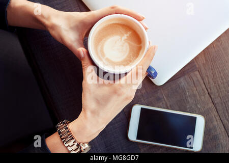 Das Mädchen hält eine Tasse Kaffee Cappuccino latte Kunst auf dem Hintergrund einer hölzernen Tisch. nach oben anzeigen Stockfoto