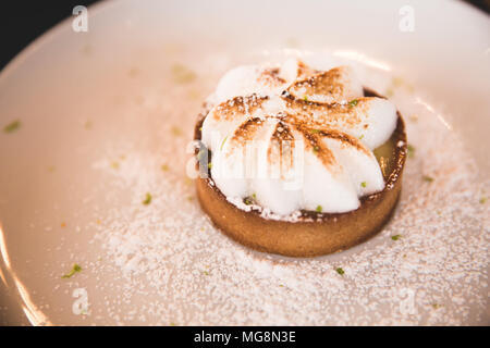 Lemon Meringue Tartelette mit Topping auf eine weisse Platte Stockfoto