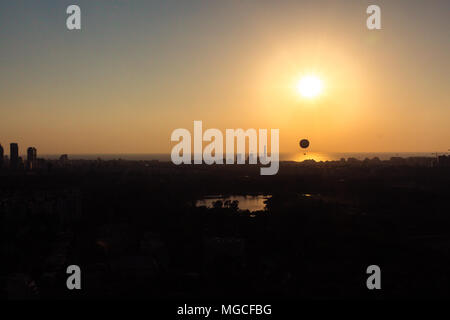 Skyline von Tel Aviv bei Sonnenuntergang - Silhouette. Sie sehen, ein Heißluftballon fliegen in der Luft. Darüber hinaus ist die Gegend im Norden von Tel Aviv sehen können, Hayarko Stockfoto