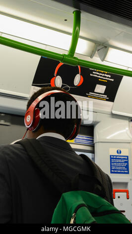 Menschen, die auf der Londoner U-Bahn, das Tragen der roten Kopfhörer, stehen unter einem Plakat werbung red Kopfhörer, Rückansicht Stockfoto