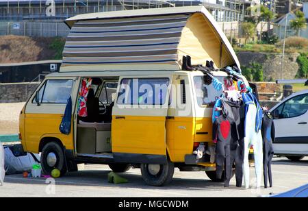 Perranporth, Cornwall, Großbritannien - 9. April 2018: Gelbe VW oder VW Wohnmobil mit Dach verlängert, mit neoprenanzügen und Surf Getriebe außen. Stockfoto