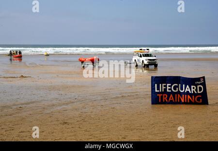 Perranporth, Cornwall, Großbritannien - 9. April 2018: RNLI lifeguards Ausbildung in der Brandung am Strand, mit Lkw, Schlauchboote und Jetskis, hinter einem großen Schild. Stockfoto