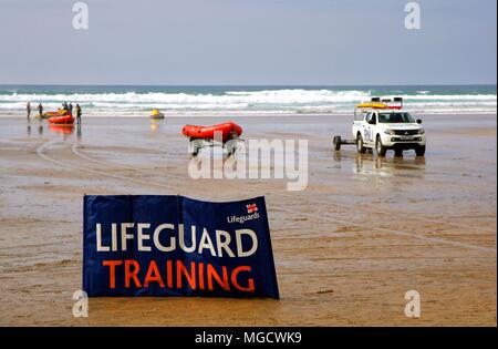 Perranporth, Cornwall, Großbritannien - 9. April 2018: RNLI lifeguards Ausbildung in der Brandung am Strand, mit Lkw, Schlauchboote und Jetskis, hinter einem großen Schild. Stockfoto