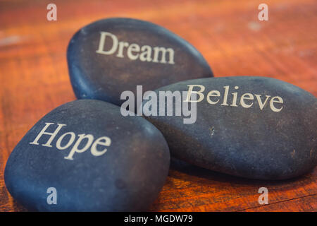 Schwarz inspirational Pebble Stones mit den Worten Traum, Glauben und Hoffen auf Holz- Hintergrund. Stockfoto
