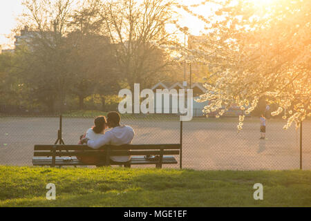 Ein interracial Paare teilen ein Getränk und jede andere Firma unter einem blühenden Kirschbaum in einem Londoner Park als die Sonne genießen geht nach unten Stockfoto