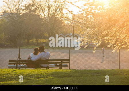 Ein interracial Paare teilen ein Getränk und jede andere Firma unter einem blühenden Kirschbaum in einem Londoner Park als die Sonne genießen geht nach unten Stockfoto