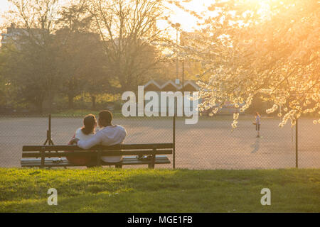 Ein interracial Paare teilen ein Getränk und jede andere Firma unter einem blühenden Kirschbaum in einem Londoner Park als die Sonne genießen geht nach unten Stockfoto