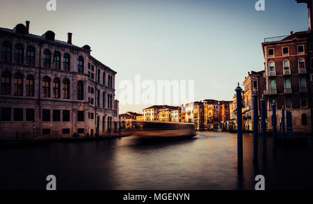 Ein Boot in Bewegung kreuzt den Canale Grande von Venedig bei Sonnenuntergang, während die Sonne die Fassade von einigen historischen Gebäuden am Ufer des Kanals hits Stockfoto