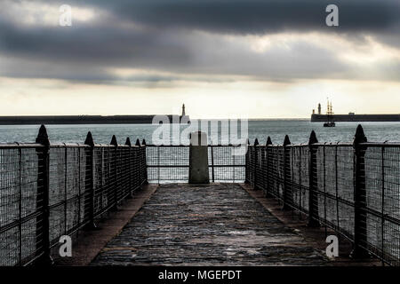 Ein Lattenrost konkrete Pier mit Blick auf die raue See von Dover in England auf einem grauen Tag, während der Himmel in den Farben gelb und weiß nimmt Stockfoto