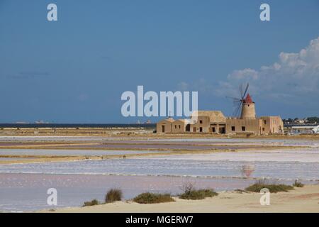 Ein weißer Leuchtturm mit einem roten Dach in der Mitte der Salinen von Marsala, Sizilien, Italien, an einem schönen sonnigen Tag mit blauem Himmel widerspiegelt Stockfoto