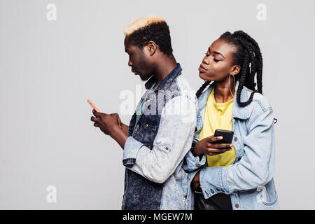 Frau versuchen Mann chatten in Handys zu sehen. Seite Portrait von afrikanischen Paar stehen Rücken an Rücken holding Handys gegen Weiße. Stockfoto