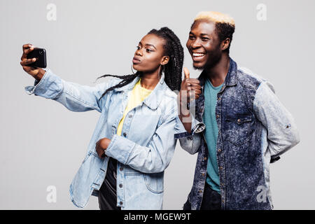 Porträt eines liebevollen jungen afrikanischen Paar umarmt, während zusammen und nehmen eine selfie über grauer Hintergrund Stockfoto